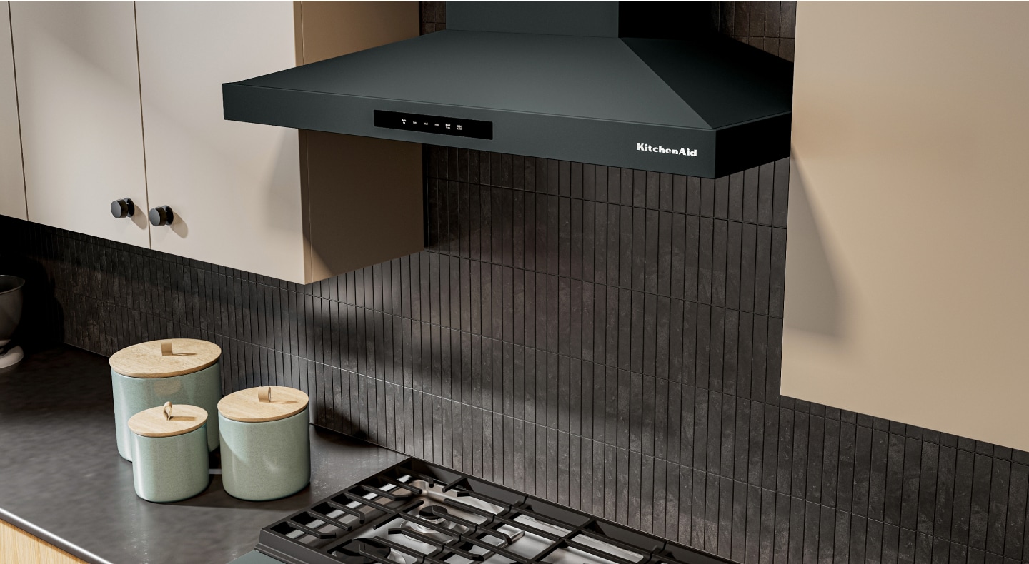 KitchenAid® Wall-Mount Range Hood in front of a gray-black backsplash