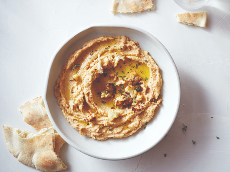 Hummus topped with herbs next to slices of pita bread Hummus topped with herbs next to slices of pita bread
