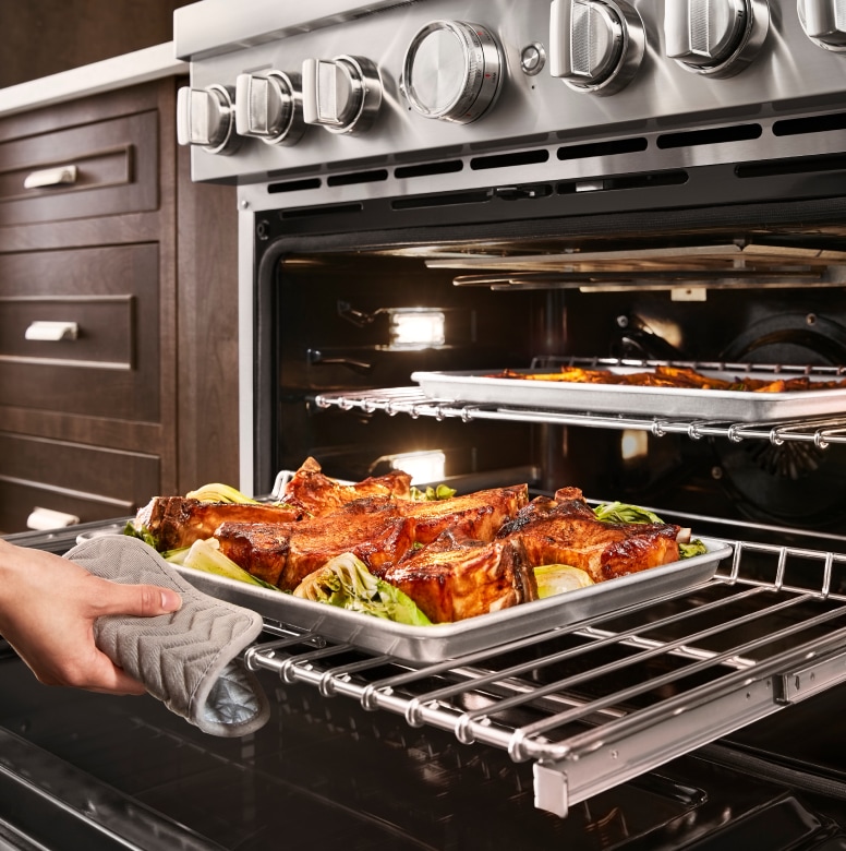 Hand removing roasted meat and vegetables from oven