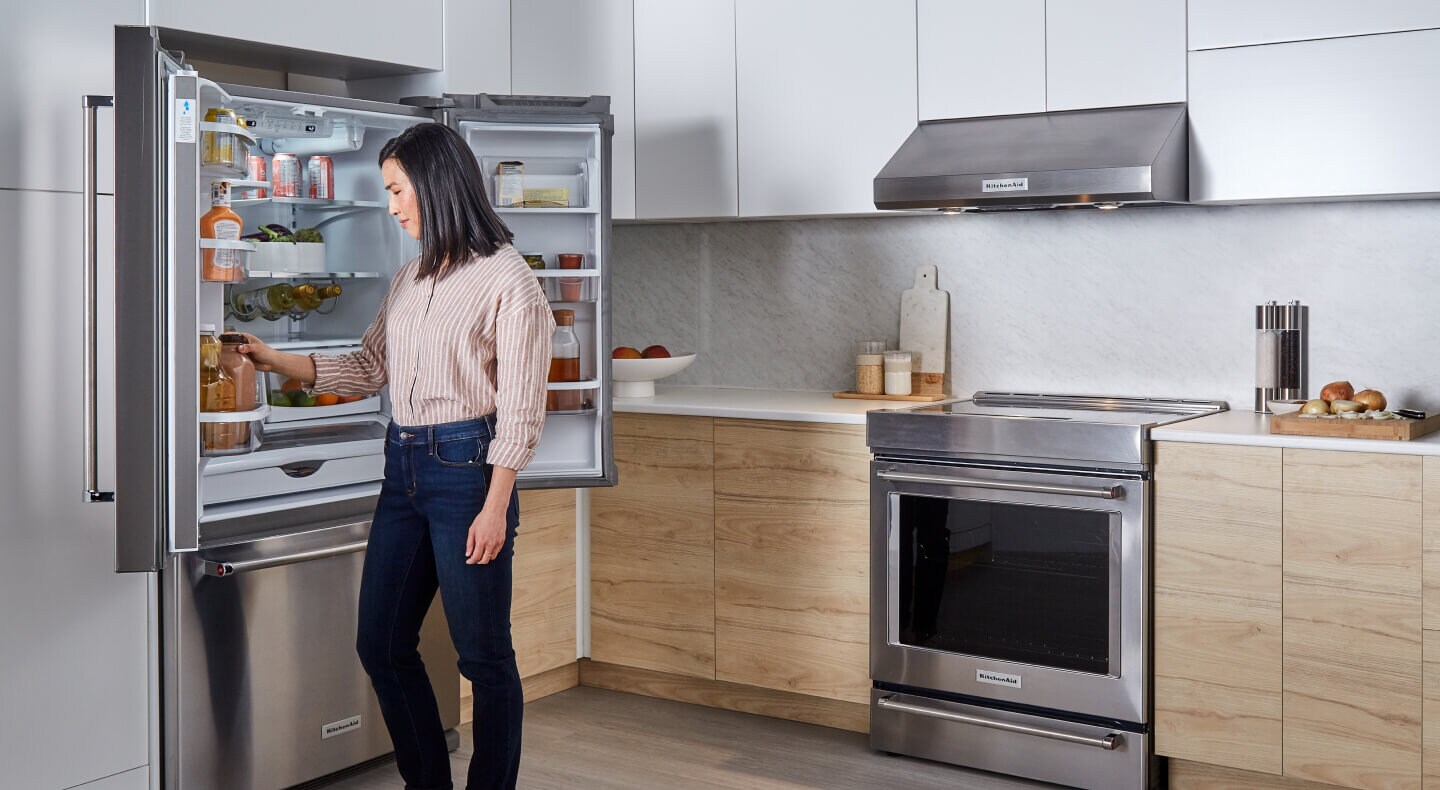 A person putting food into a refrigerator with both doors open A person putting food into a refrigerator with both doors open