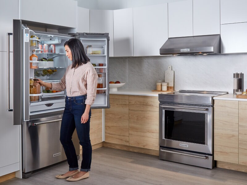 A person putting food into a refrigerator with both doors open A person putting food into a refrigerator with both doors open