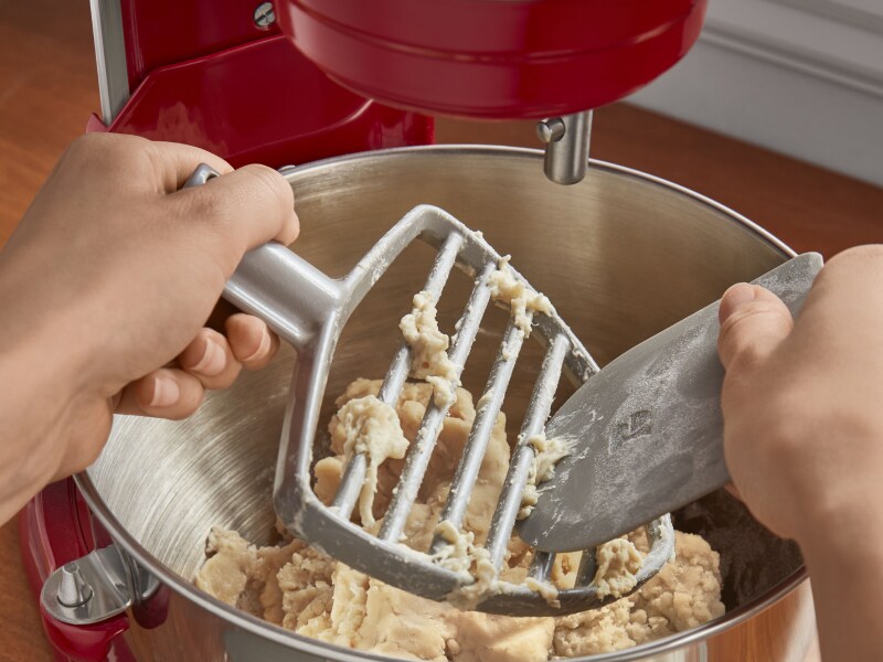 Hand cleaning off the KitchenAid® Pastry Beater Accessory above bowl of dough