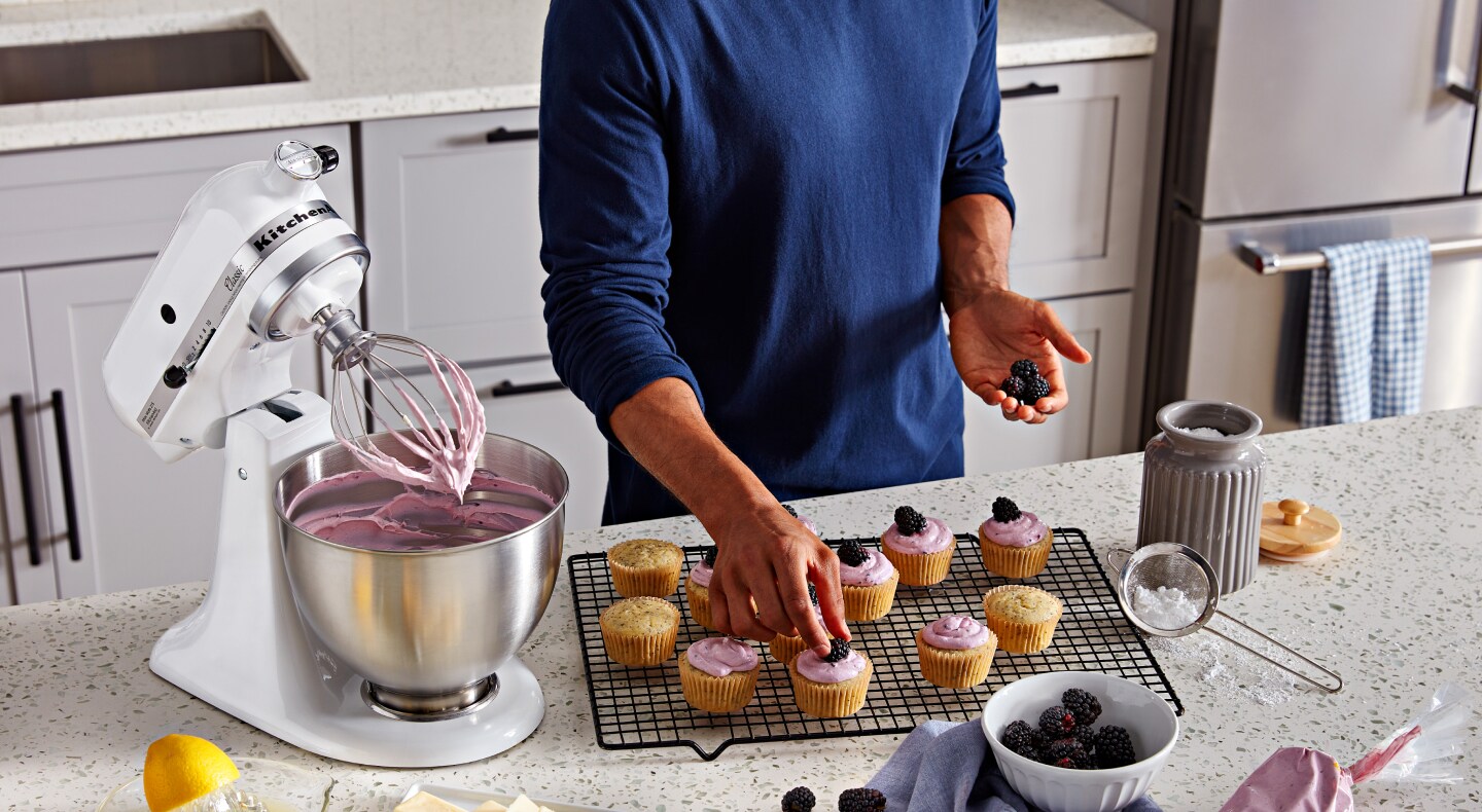 White KitchenAid® stand mixer next to person putting toppings on cupcakes White KitchenAid® stand mixer next to person putting toppings on cupcakes