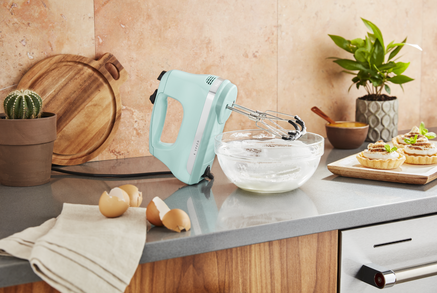 Light pistachio green KitchenAid® hand mixer on countertop with egg shells and bowl of whisked egg whites Light pistachio green KitchenAid® hand mixer on countertop with egg shells and bowl of whisked egg whites