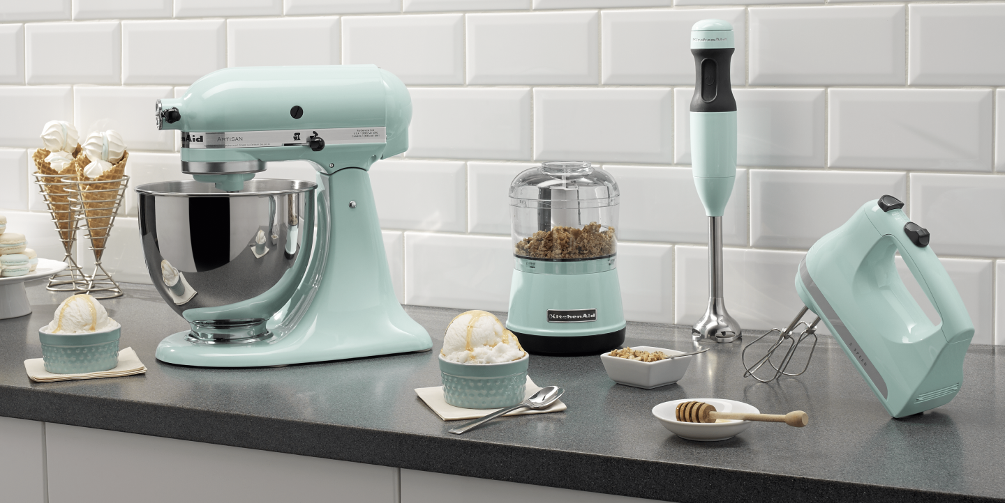 Mint green KitchenAid® food processor, stand mixer, hand mixer and immersion blender on countertop with ingredients Mint green KitchenAid® food processor, stand mixer, hand mixer and immersion blender on countertop with ingredients