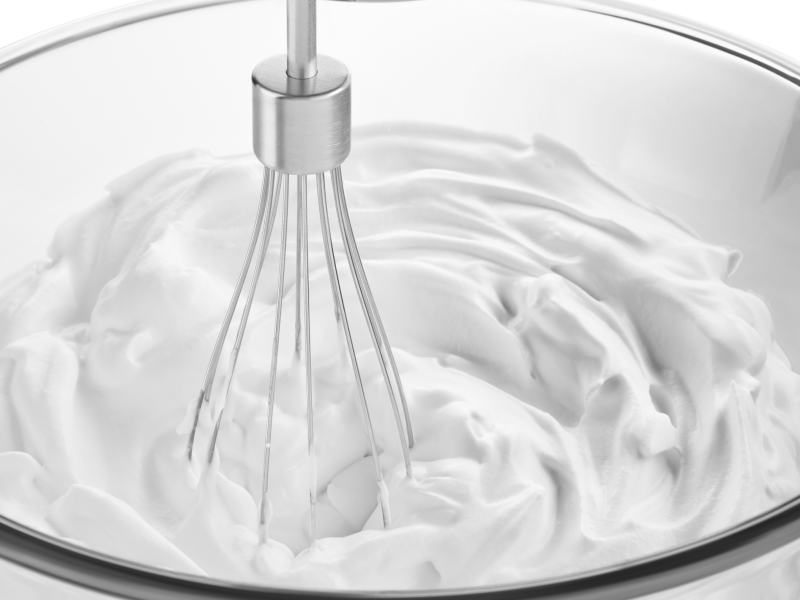 Close up of wire whisk beating white cream in glass bowl