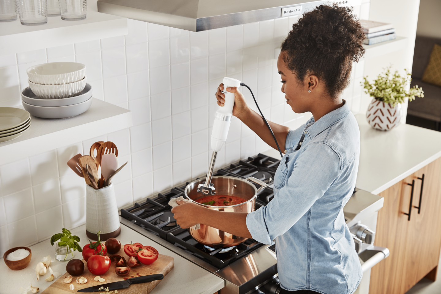 Maker using KitchenAid® immersion blender to mix ingredients in pot on top of stovetop Maker using KitchenAid® immersion blender to mix ingredients in pot on top of stovetop