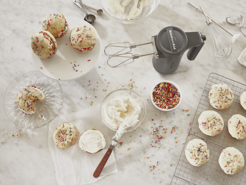 Gray KitchenAid® hand mixer standing upright on countertop along with sandwich cookies, frosting, sprinkles and beater accessories Gray KitchenAid® hand mixer standing upright on countertop along with sandwich cookies, frosting, sprinkles and beater accessories