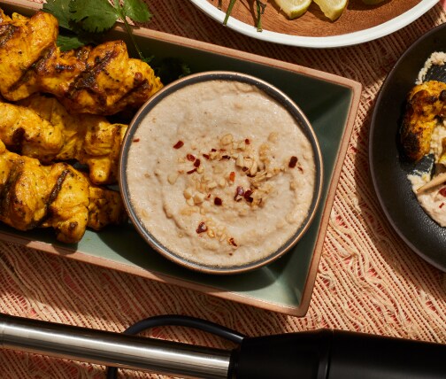 Immersion blender on table with satay chicken and sauce