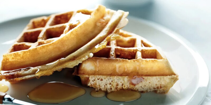 Two quarters of waffles sitting on a plate, drizzled with syrup. Two quarters of waffles sitting on a plate, drizzled with syrup.