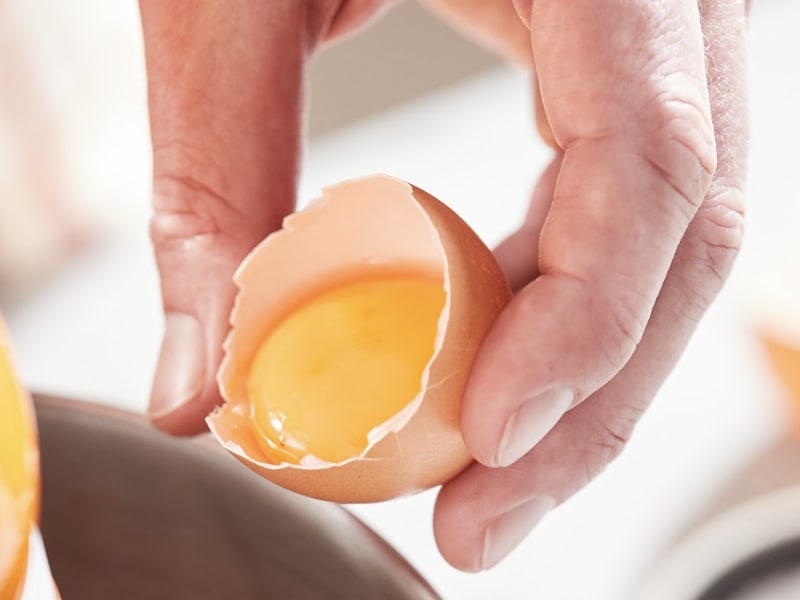 A person holding a cracked egg shell with yolk inside