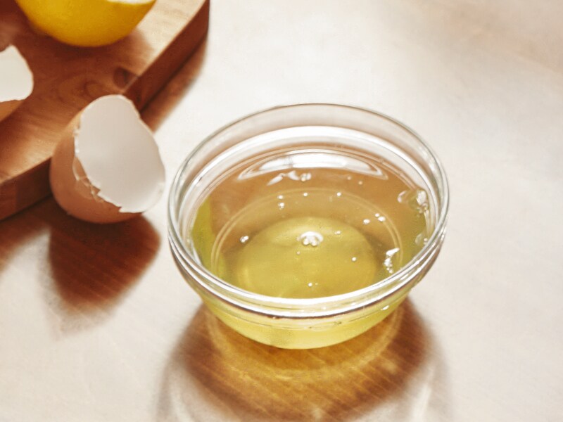 A cup of oil next to cracked eggs