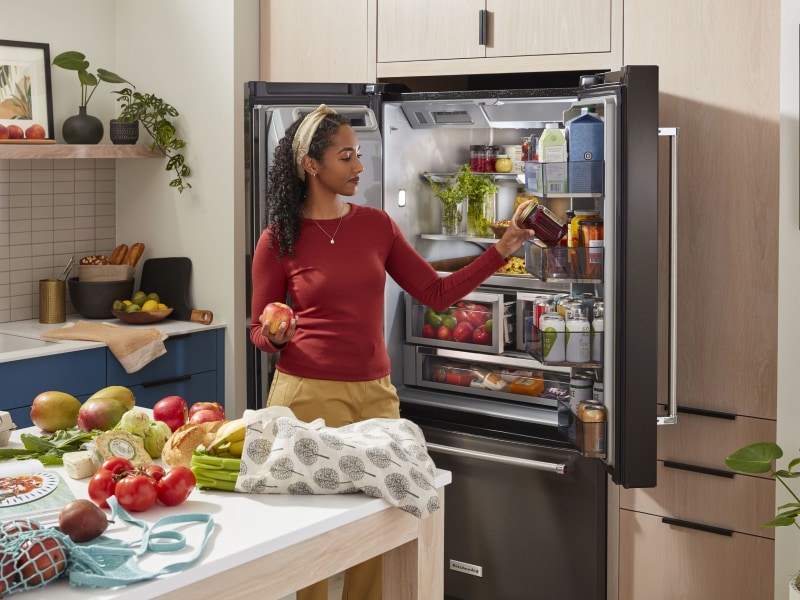 Person putting items in a KitchenAid® French door refrigerator near ingredients on counter Person putting items in a KitchenAid® French door refrigerator near ingredients on counter