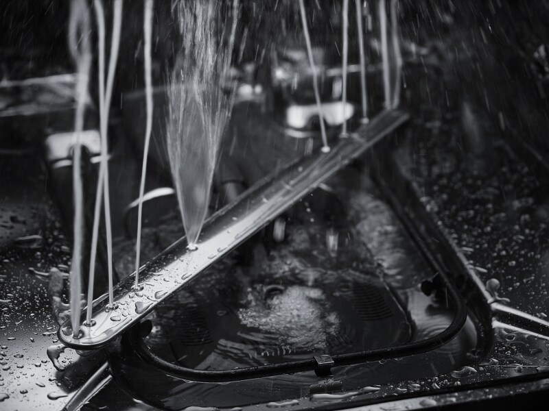 A closeup of a spray arm at the base of a KitchenAid® dishwasher spraying water.
