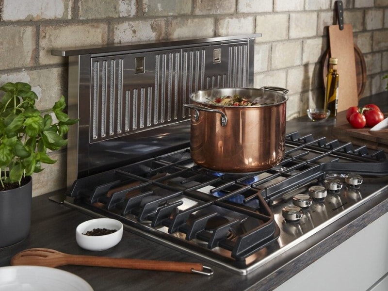 Stock pot on lit gas burner in front of a downdraft range hood