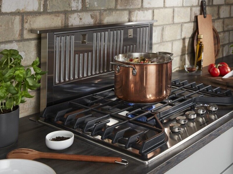 Stock pot on lit gas burner in front of a downdraft range hood