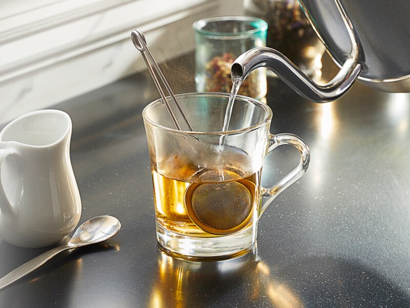 Gooseneck kettle pouring water into a glass mug to steep tea