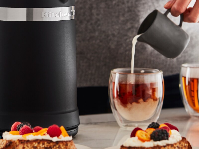 Person pouring steamed milk into glass mugs of tea