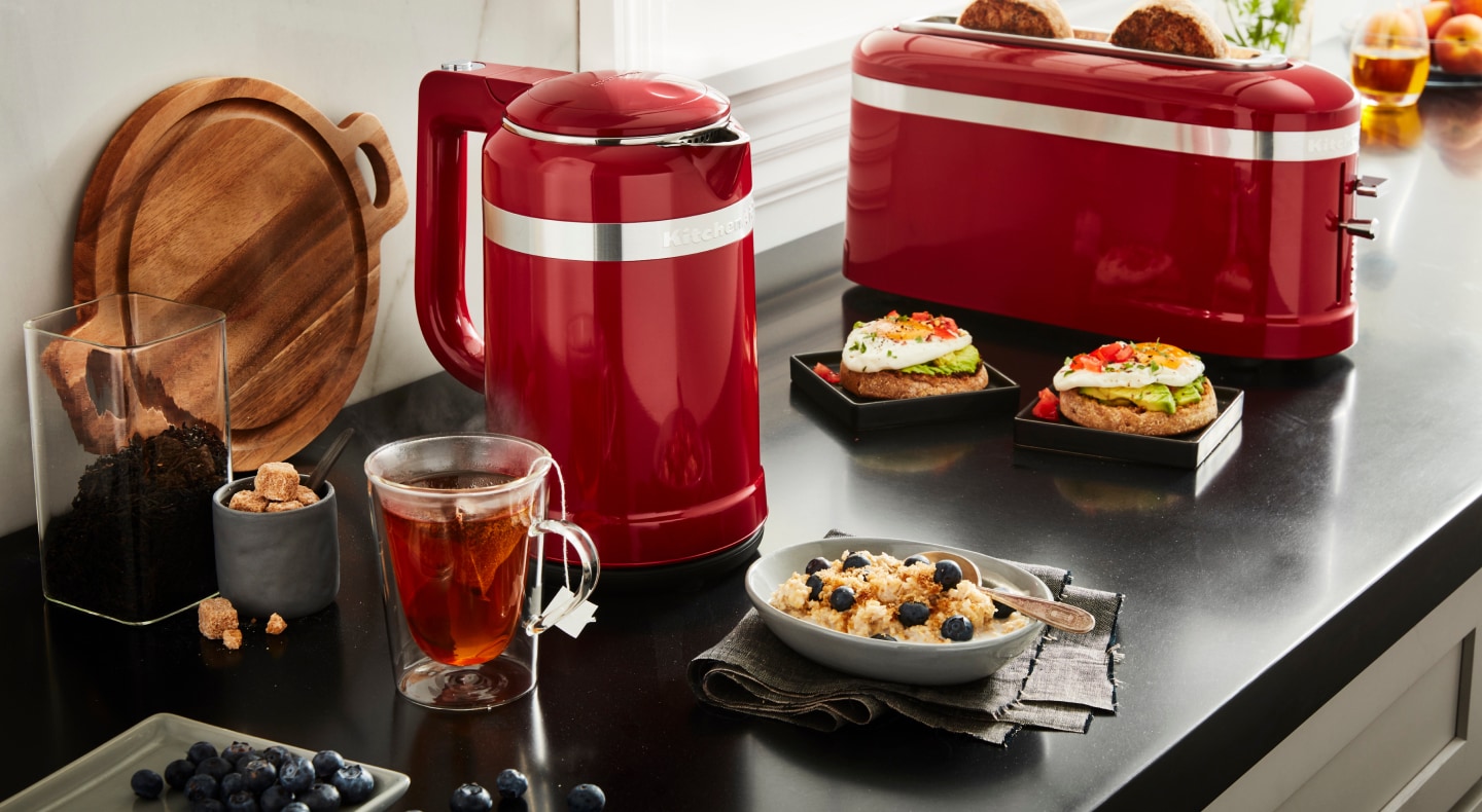 Red KitchenAid® electric kettle and toaster next to breakfast and tea