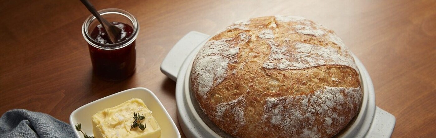 A round loaf of crusty bread with butter and honey on the side