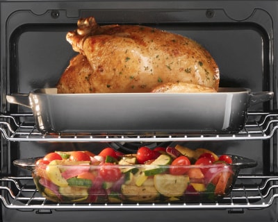 Two oven racks holding a turkey in a dish and a casserole of vegetables