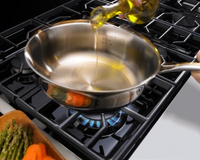 Bottle of oil being poured into a pan on a cooktop