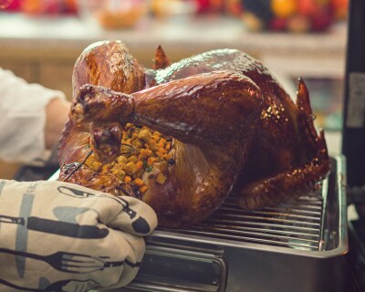 Oven mitt hands pulling a roasted turkey out of the oven