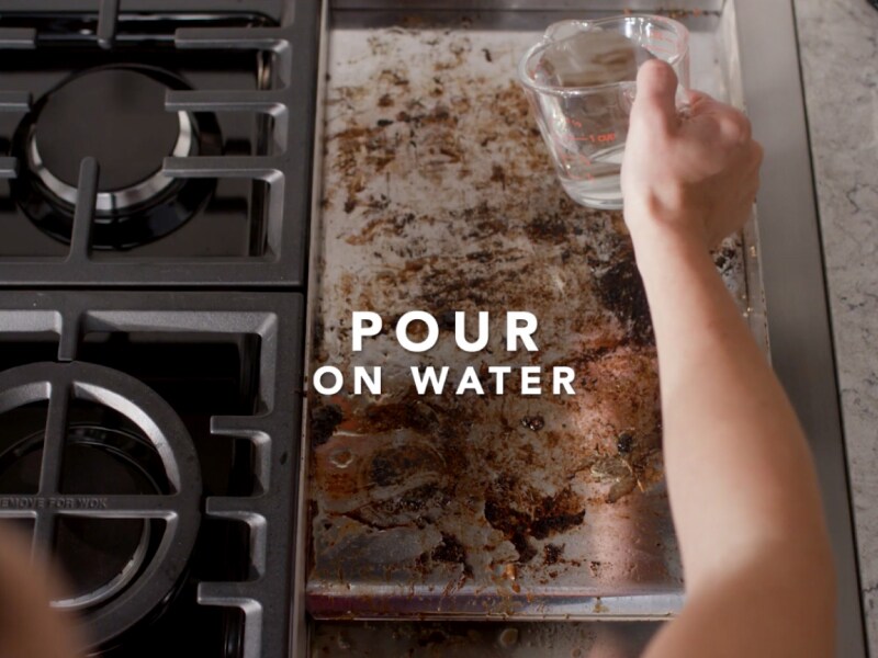 Person pouring water on dirty griddle 
