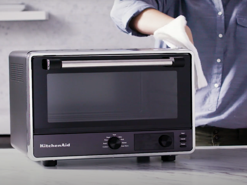 A person cleaning the exterior of a black KitchenAid® air fryer
