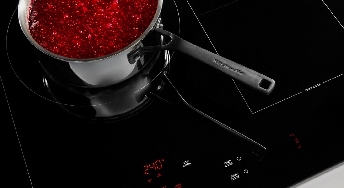A KitchenAid® sauce pot filled with red jam on an induction cooktop