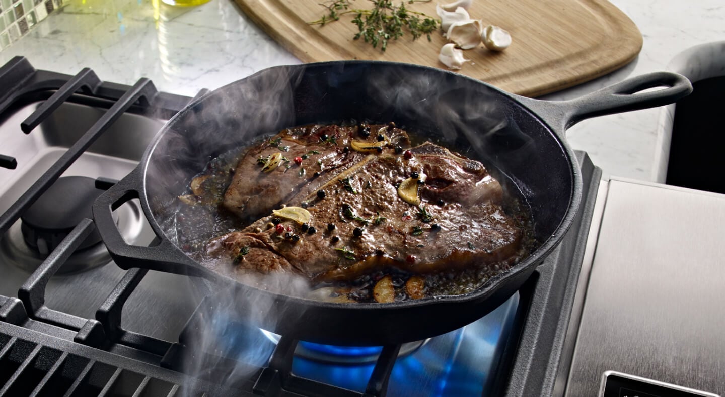 Steak cooking in a cast iron skillet in a kitchen with granite countertops. Steak cooking in a cast iron skillet in a kitchen with granite countertops.