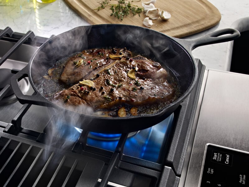 Steak cooking in a cast iron skillet in a kitchen with granite countertops. Steak cooking in a cast iron skillet in a kitchen with granite countertops.