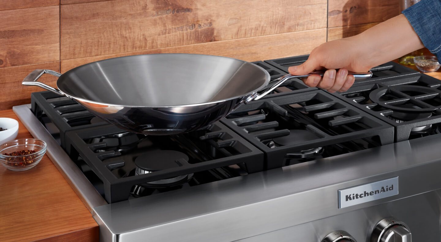 Person holding a wok over a KitchenAid® brand gas range Person holding a wok over a KitchenAid® brand gas range