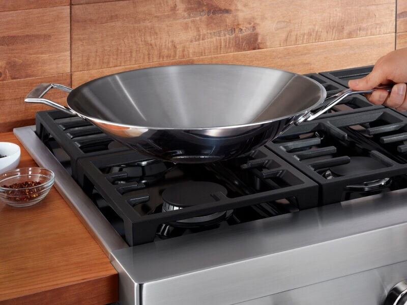 Person holding a wok over a KitchenAid® brand gas range Person holding a wok over a KitchenAid® brand gas range