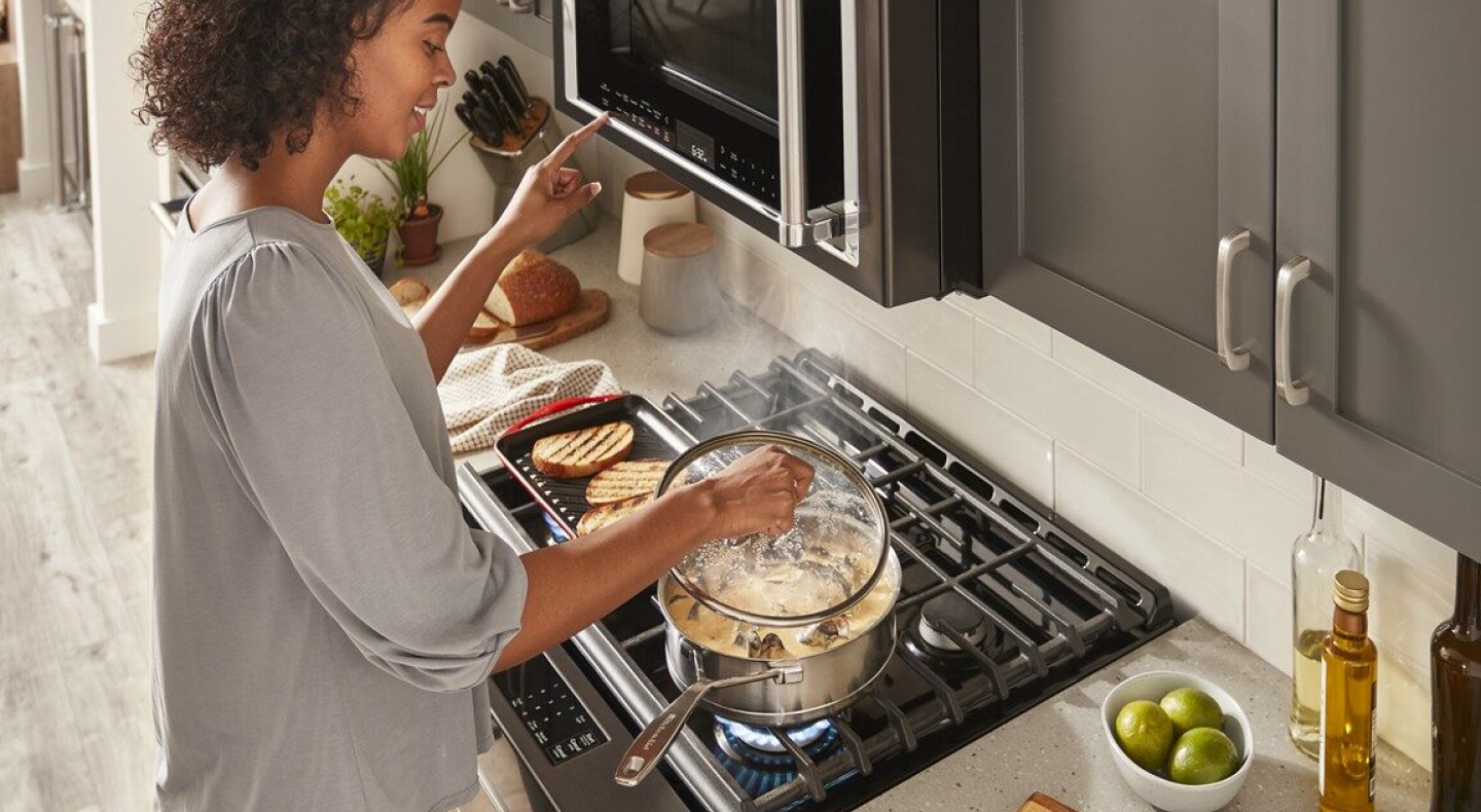 A person preparing a meal on a KitchenAid® gas stovetop.