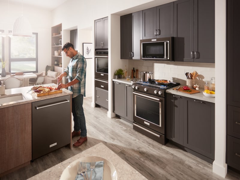 A man chopping ingredients in front of a KitchenAid® slide-in range and microwave A man chopping ingredients in front of a KitchenAid® slide-in range and microwave