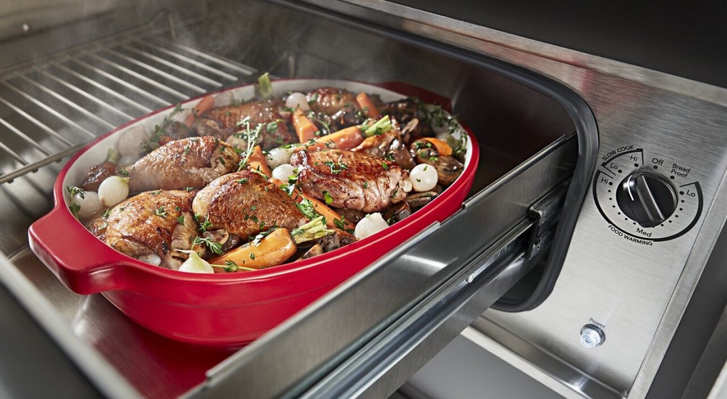 Roasted chicken thighs and vegetables in a casserole dish inside of a warming drawer Roasted chicken thighs and vegetables in a casserole dish inside of a warming drawer