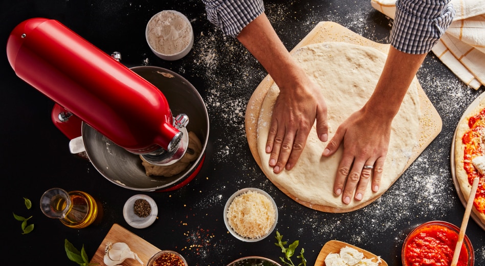 Two hands pushing down circle of dough on pizza peel next to red KitchenAid® Stand Mixer Two hands pushing down circle of dough on pizza peel next to red KitchenAid® Stand Mixer