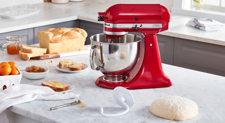 Red KitchenAid® Stand Mixer on countertop next to a baked loaf of bread, dough hook accessory and ball of dough Red KitchenAid® Stand Mixer on countertop next to a baked loaf of bread, dough hook accessory and ball of dough