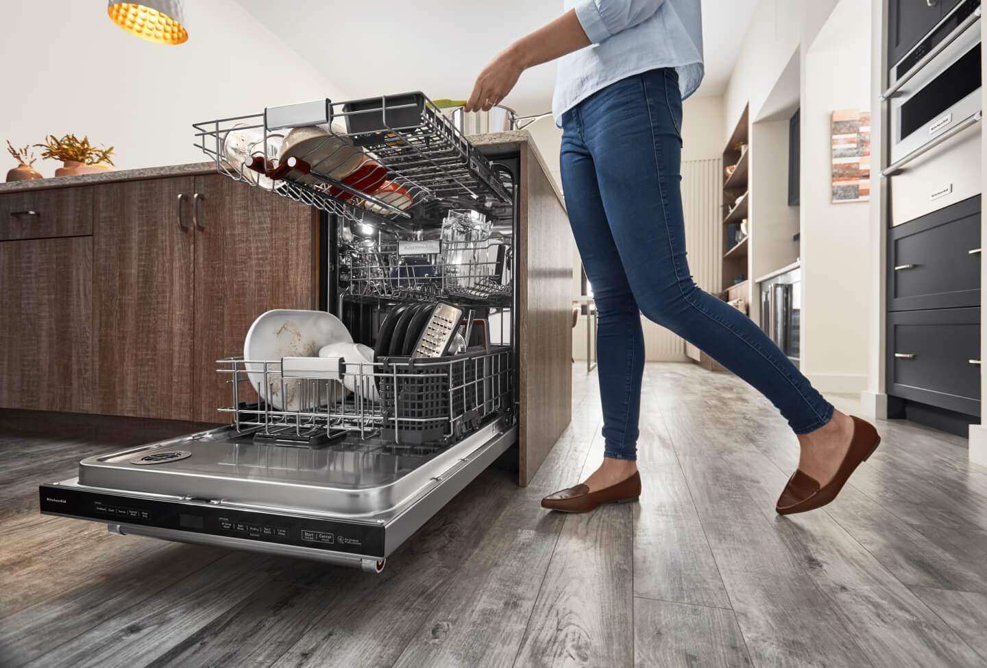 Person in a kitchen loading dirty plates into a dishwasher
