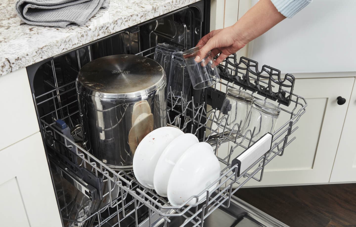 Person placing a glass cup into a dishwasher Person placing a glass cup into a dishwasher