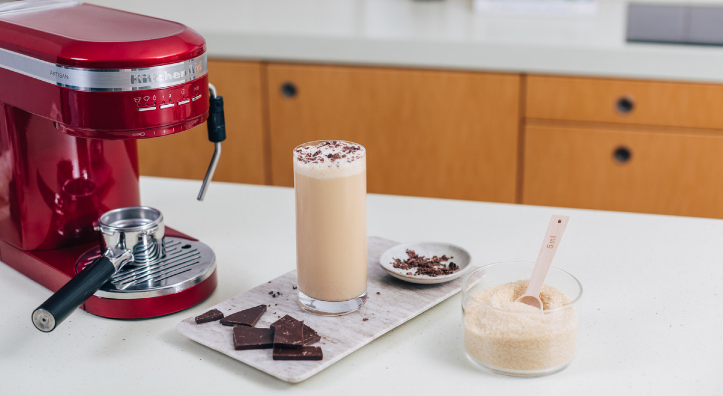 Frappe topped with chocolate shavings next to a KitchenAid® espresso machine Frappe topped with chocolate shavings next to a KitchenAid® espresso machine