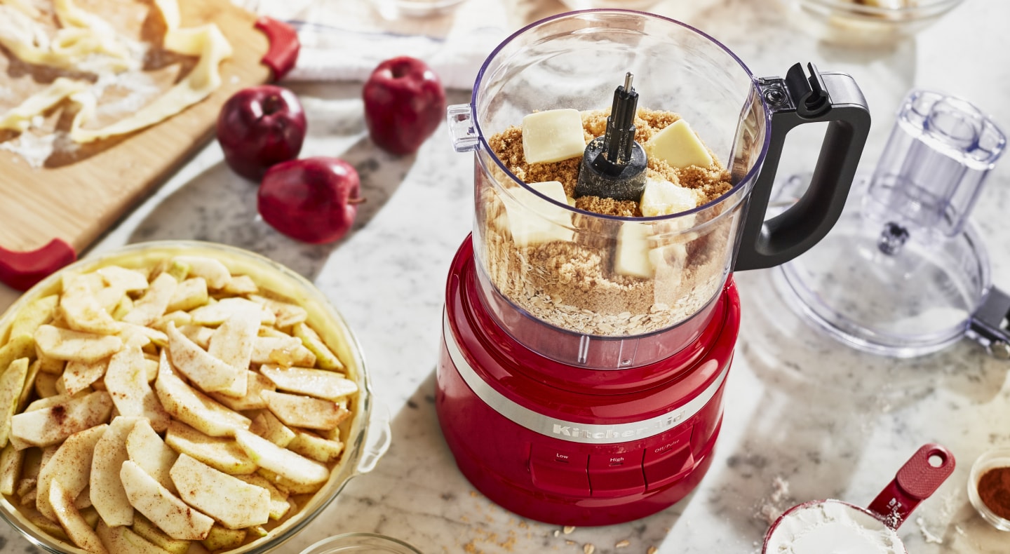 Crushed graham crackers and butter inside a KitchenAid® food processor next to an apple pie Crushed graham crackers and butter inside a KitchenAid® food processor next to an apple pie