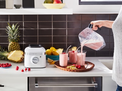 Person pouring strawberry milkshake from blender into glasses