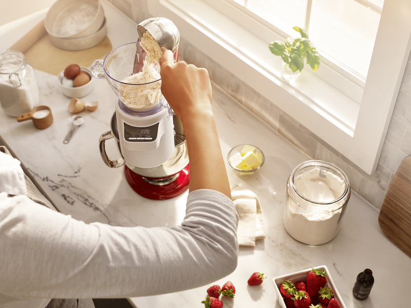 A woman adding flour to the KitchenAid® stand mixer sifter + scale attachment. A woman adding flour to the KitchenAid® stand mixer sifter + scale attachment.