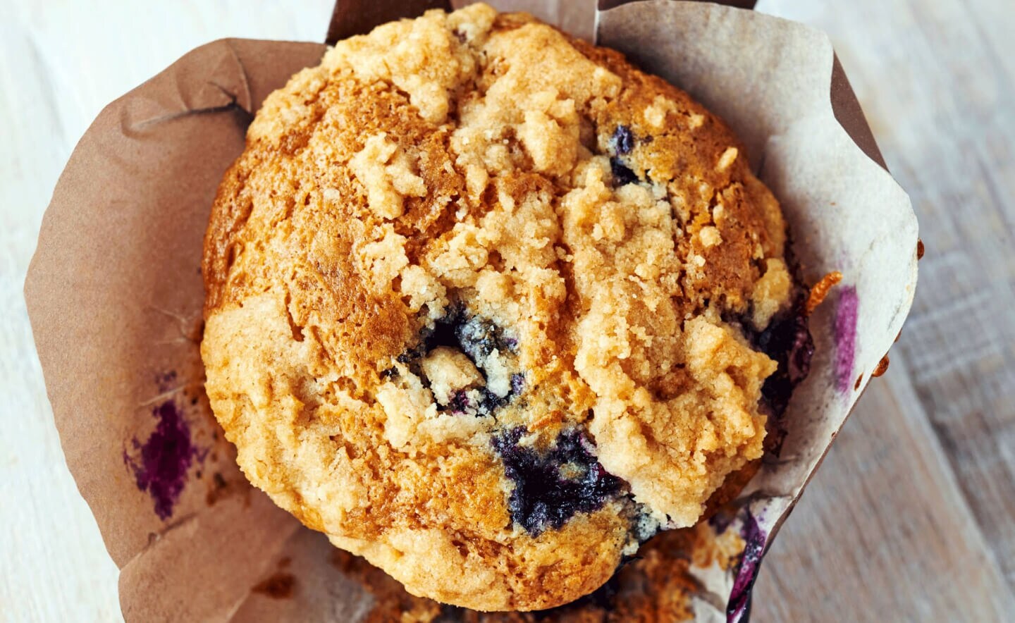 Birds-eye view of a streusel-topped blueberry muffin inside of a decorative liner Birds-eye view of a streusel-topped blueberry muffin inside of a decorative liner
