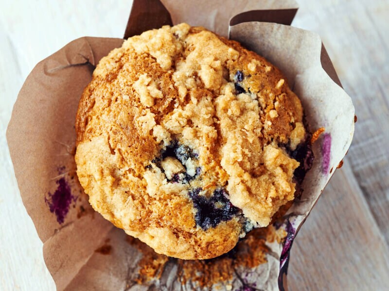 Birds-eye view of a streusel-topped blueberry muffin inside of a decorative liner Birds-eye view of a streusel-topped blueberry muffin inside of a decorative liner
