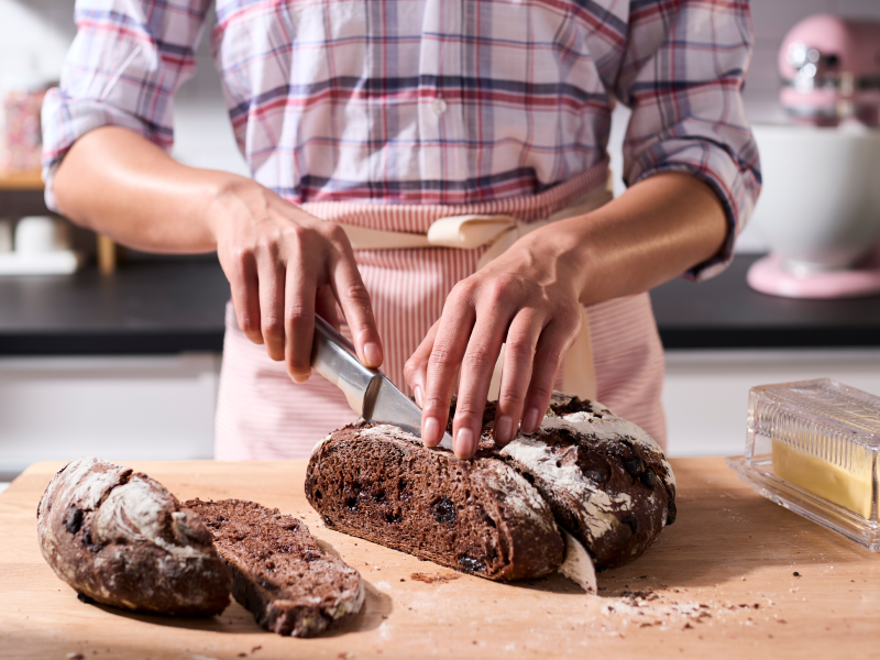 Person slicing a loaf of bread on a wooden cutting board Person slicing a loaf of bread on a wooden cutting board