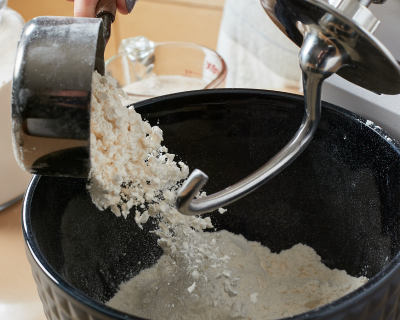 Flour pouring into a stand mixer bowl with a dough hook