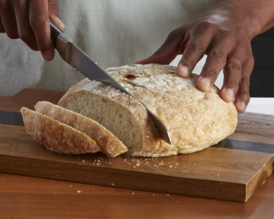 Person slicing a loaf of bread on a cutting board